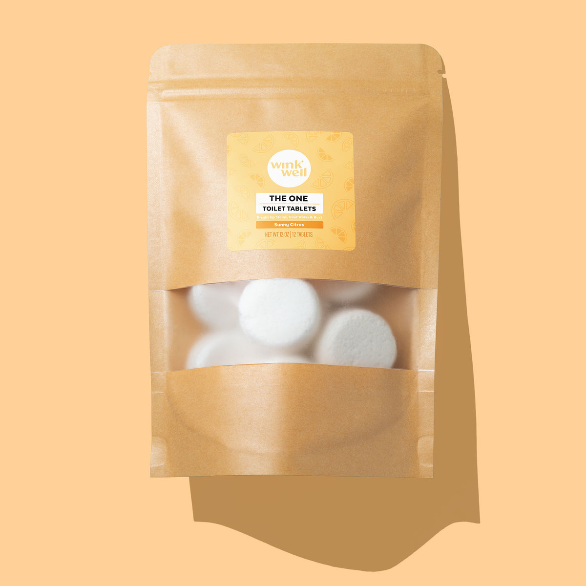 Kraft pouch of Wink Well The One Toilet Tablets in Sunny Citrus scent, white tablets visible through the window, on a warm yellow background