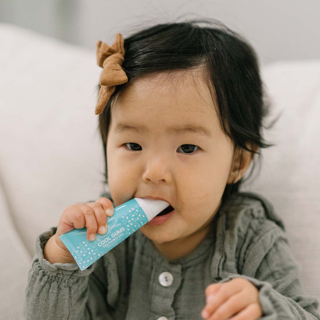Toddler in a green dress chewing on a tube of Wink Kids Cool Gums Teething Gel