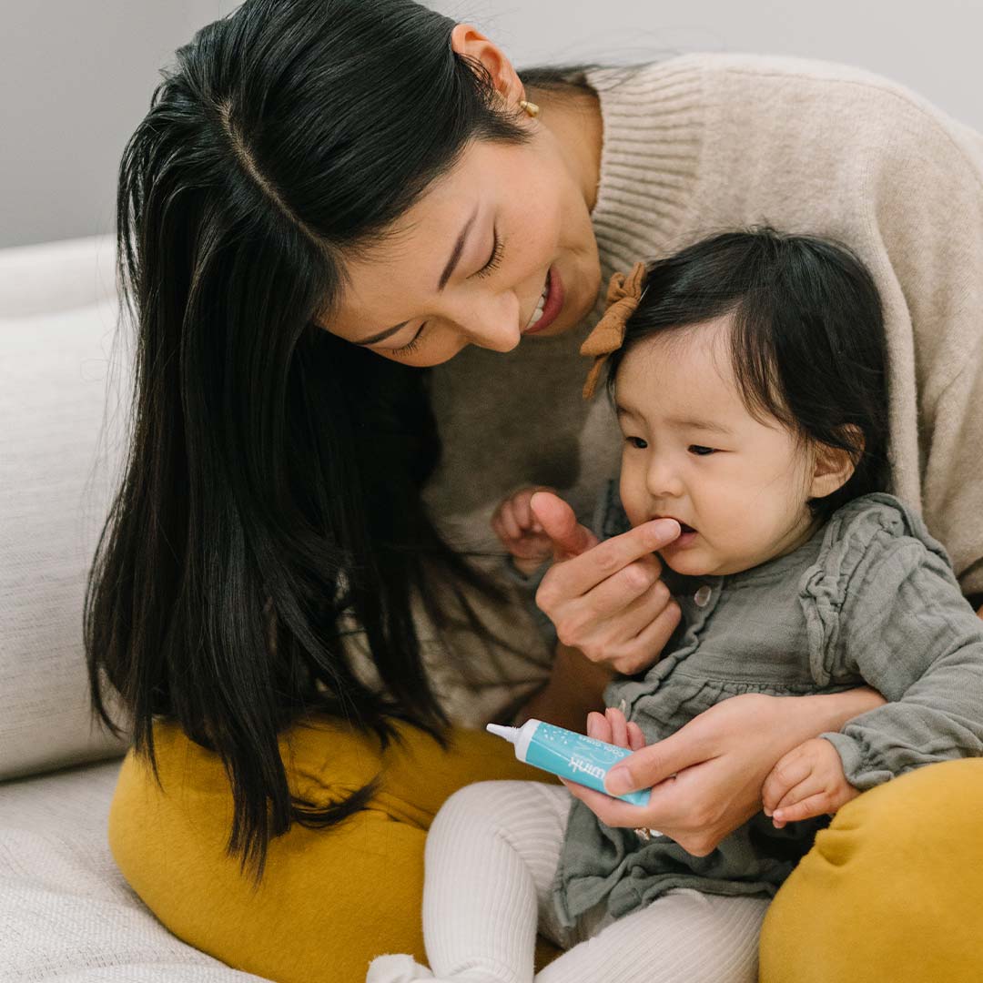 Mother smiling as she applies Wink Kids Cool Gums Teething Gel to her toddler's gums