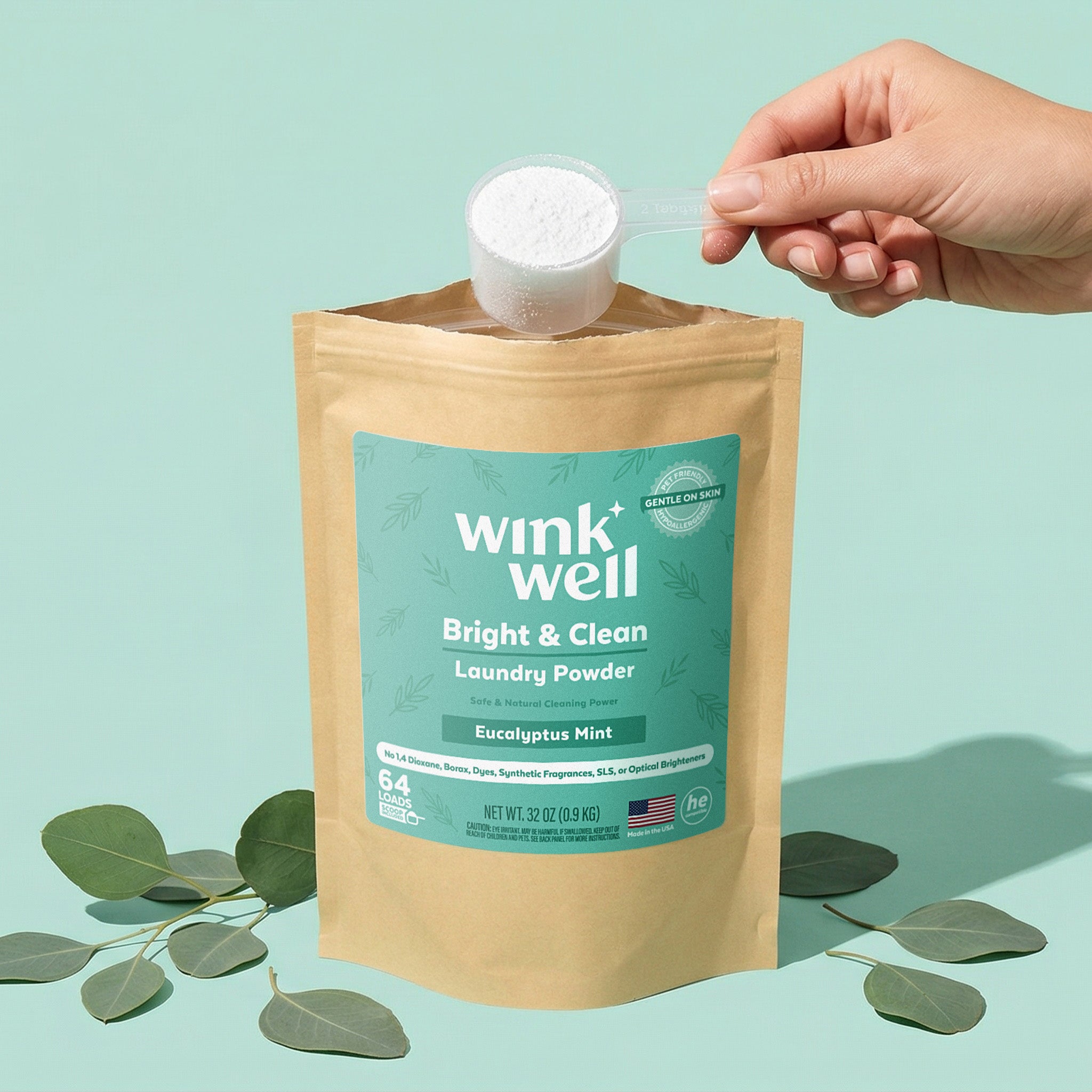 Wink Well laundry powder packaging with a hand pouring powder, on a light green background with eucalyptus leaves.