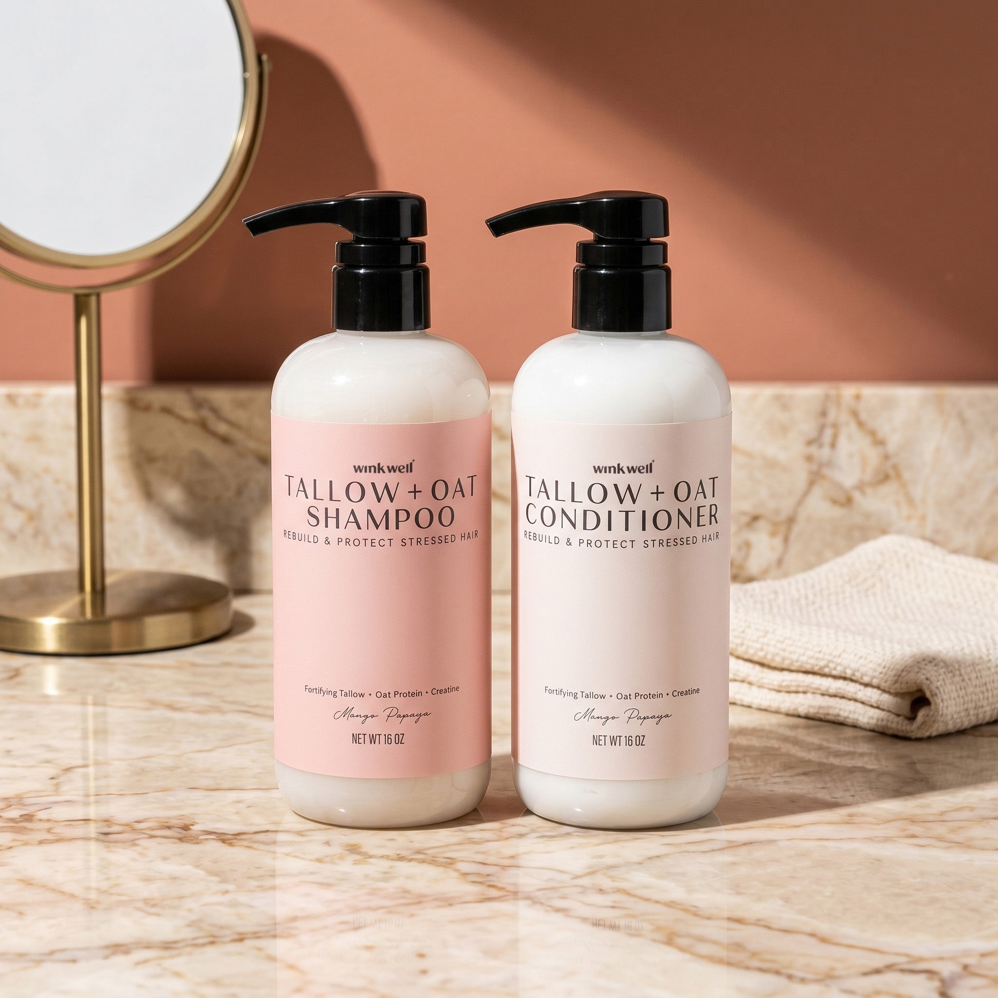 Two bottles of Wink Well Tallow + Oat shampoo and conditioner on a marble surface with a mirror in the background.