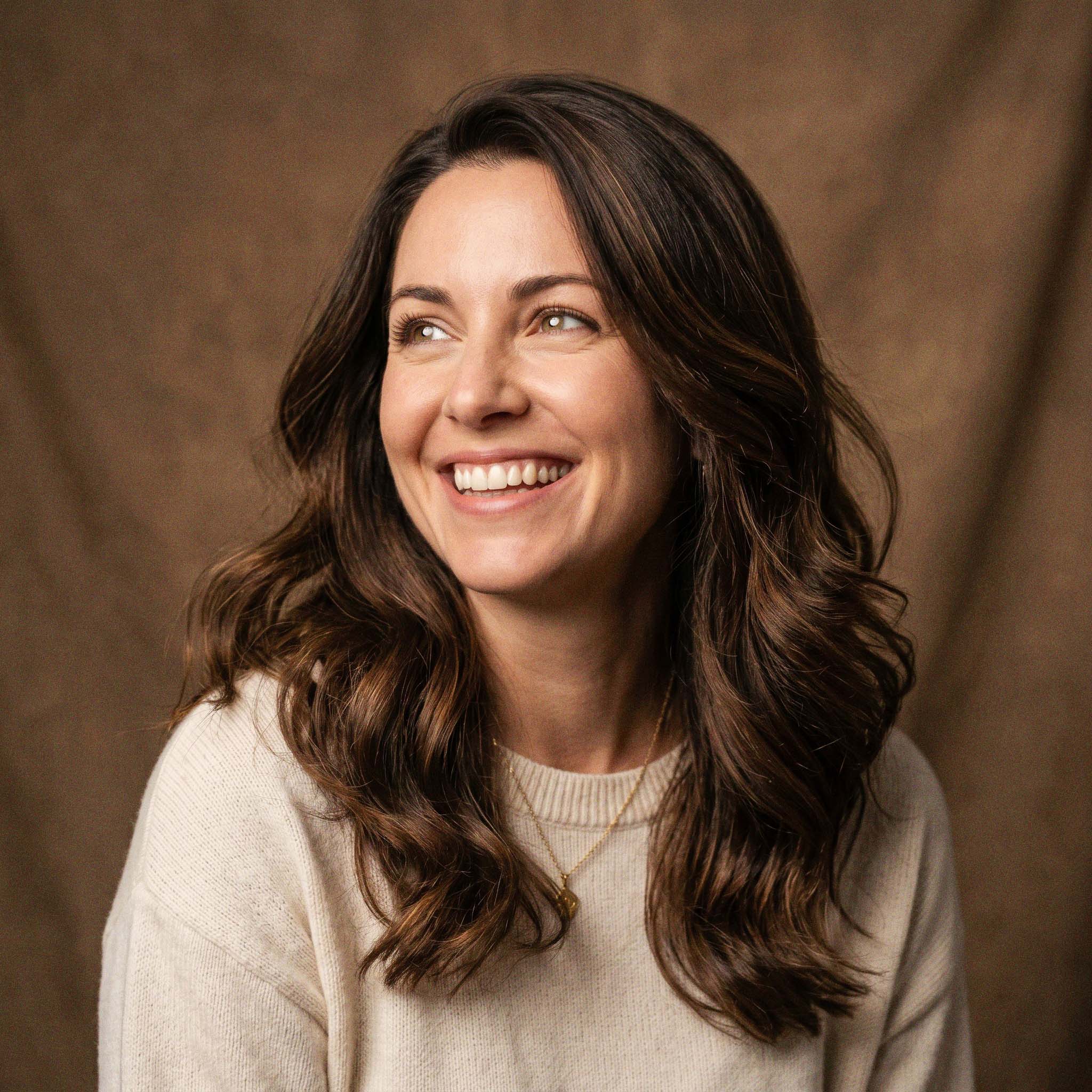 Woman with long brown hair smiling against a brown background