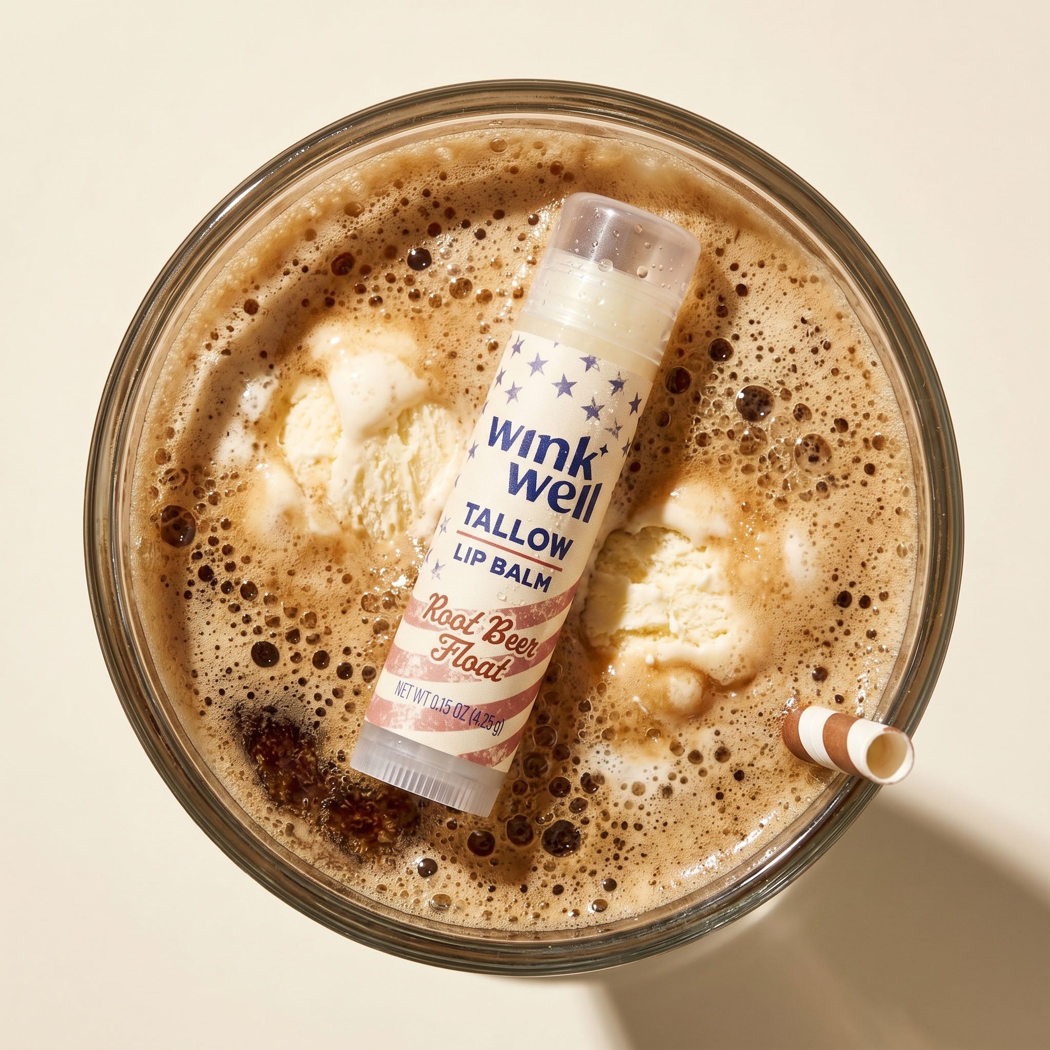 Wink Well Tallow Lip Balm in a root beer float with ice cream and a straw on a beige background, with  a patriotic American stars and stripes design.