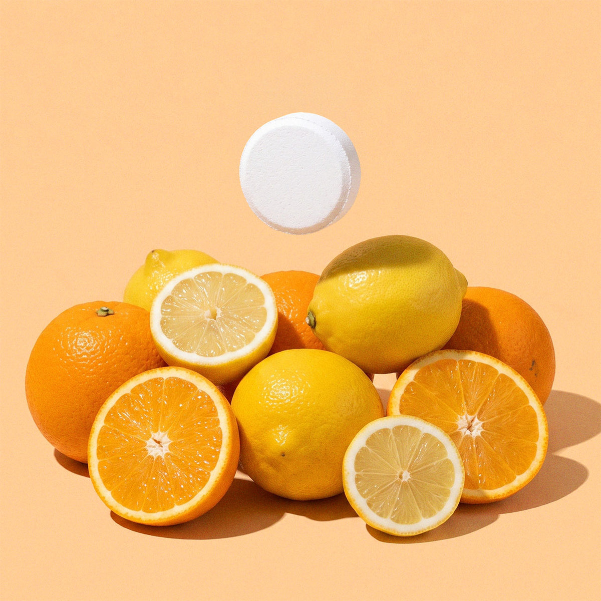 A pile of citrus fruits including whole oranges, lemons, and orange slices, with a white Wink Well Toilet Tablet floating above on a solid peach background.