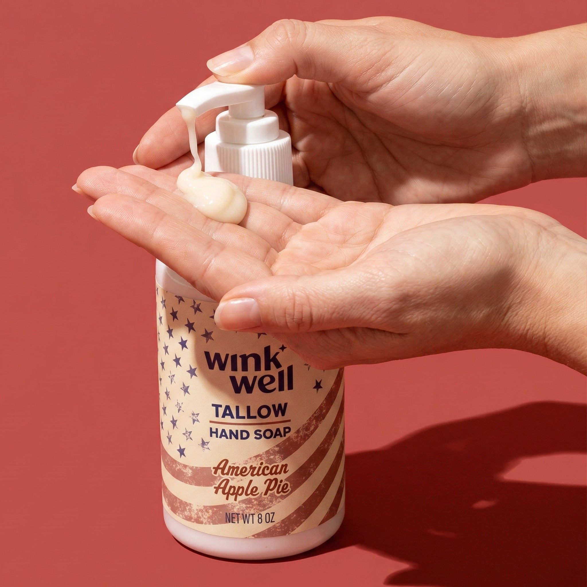 Person holding a bottle of wink well tallow hand soap in apple pie scent, with a red background