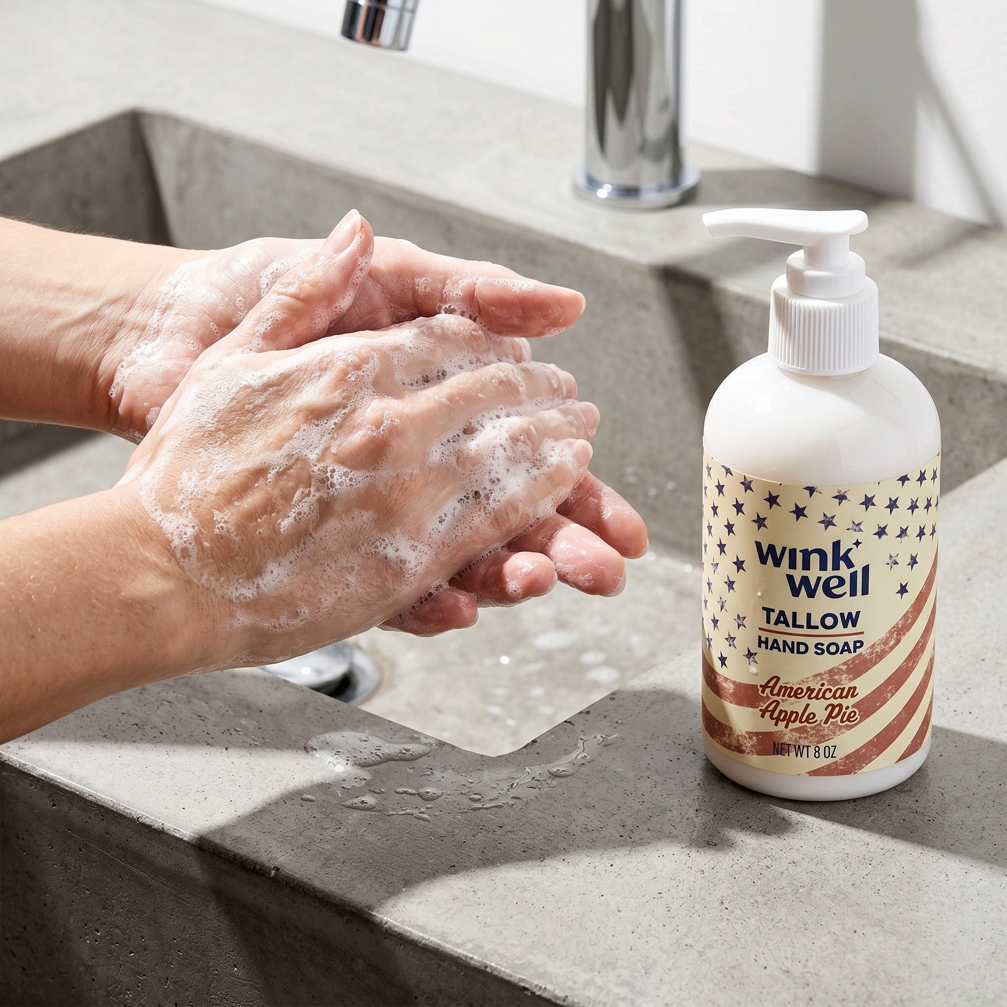Person washing hands with Wink Well Tallow Hand Soap next to a sink. The bottle is apple pie scent, with a patriotic American stars and stripes design.